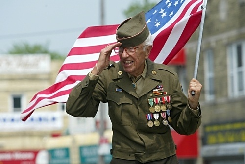 As we express our gratitude, we must never forget that the highest appreciation is not to utter words, but to live by them, image of senior veteran carrying US flag and saluting