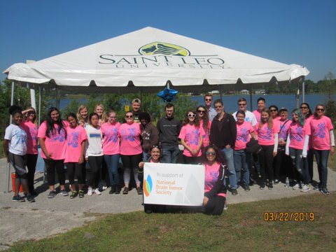 A group photo of several participants in the 5K walk wearing pink brain tumor awareness shirts and standing in front of a Saint Leo tent