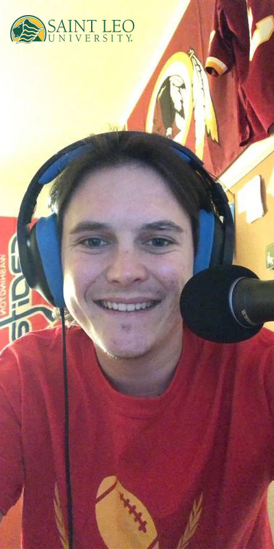 A photo of Jarret Brightbill who was a student in the podcast course at Saint Leo University in the fall of 2020 wearing headphones with a microphone in front of him as he smiles