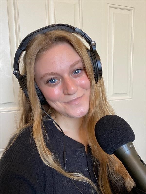 A photo of Kacie Parrow who was a student in the podcast course at Saint Leo University in the fall of 2020 wearing headphones with a microphone in front of her as she smiles