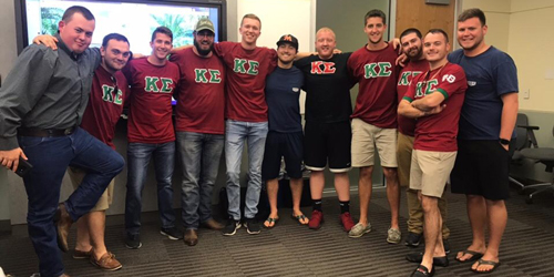 A photo of Saint Leo University alum Mike Williams standing with several fellow Kappa Sigma fraternity brothers in a classroom, and most of them are wearing their Kappa Sigma fraternity shirts