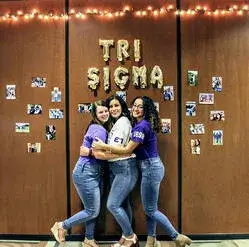 A photo of three Sigma Sigma Sigma sorority sisters hugging and posing for a picture together in the board rooms at Saint Leo’s University Campus 