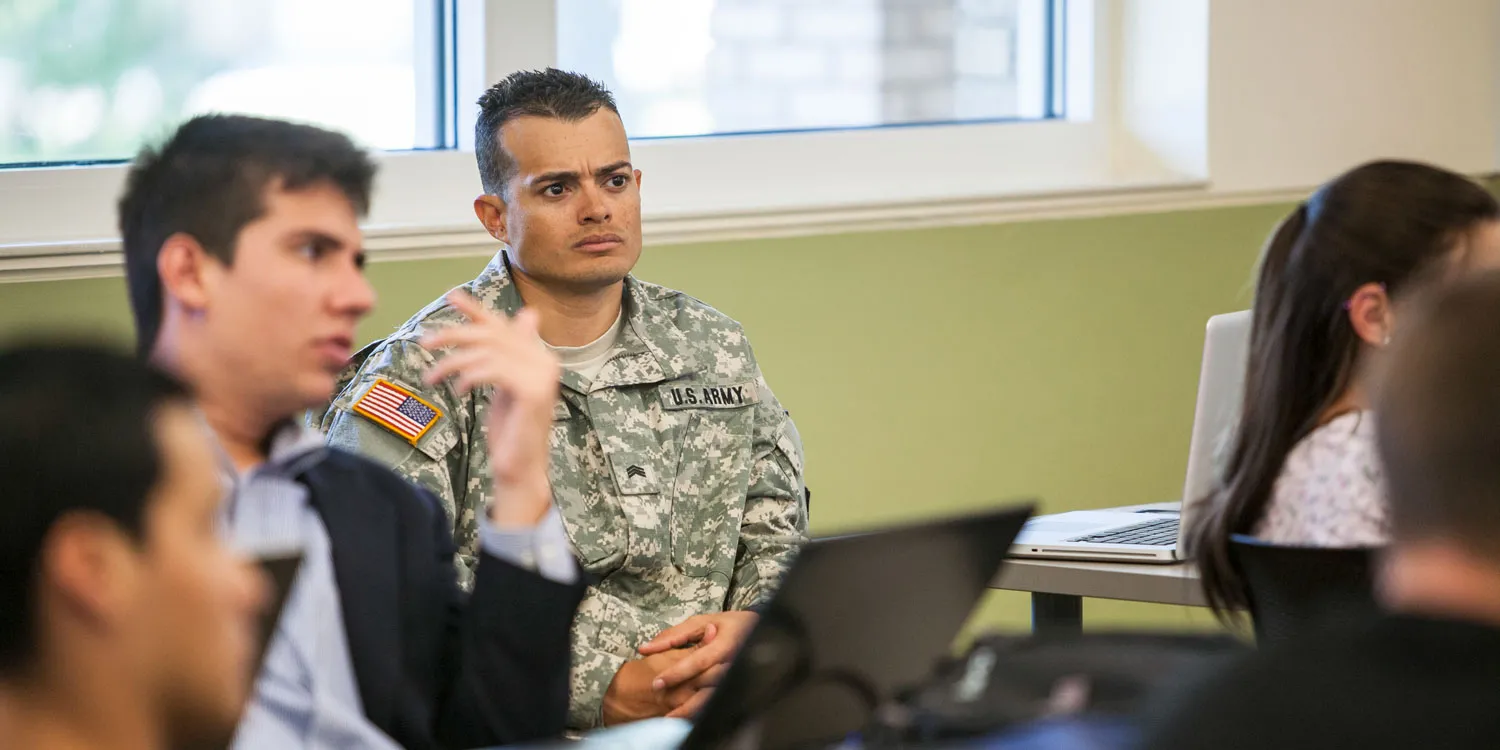 A photo of a U.S. Army soldier in uniform taking a course in a college classroom for the blog article on 'How does the Post-9/11 GI Bill work?' highlighting the eligibility requirements of this financial aid benefit for military-connected college students