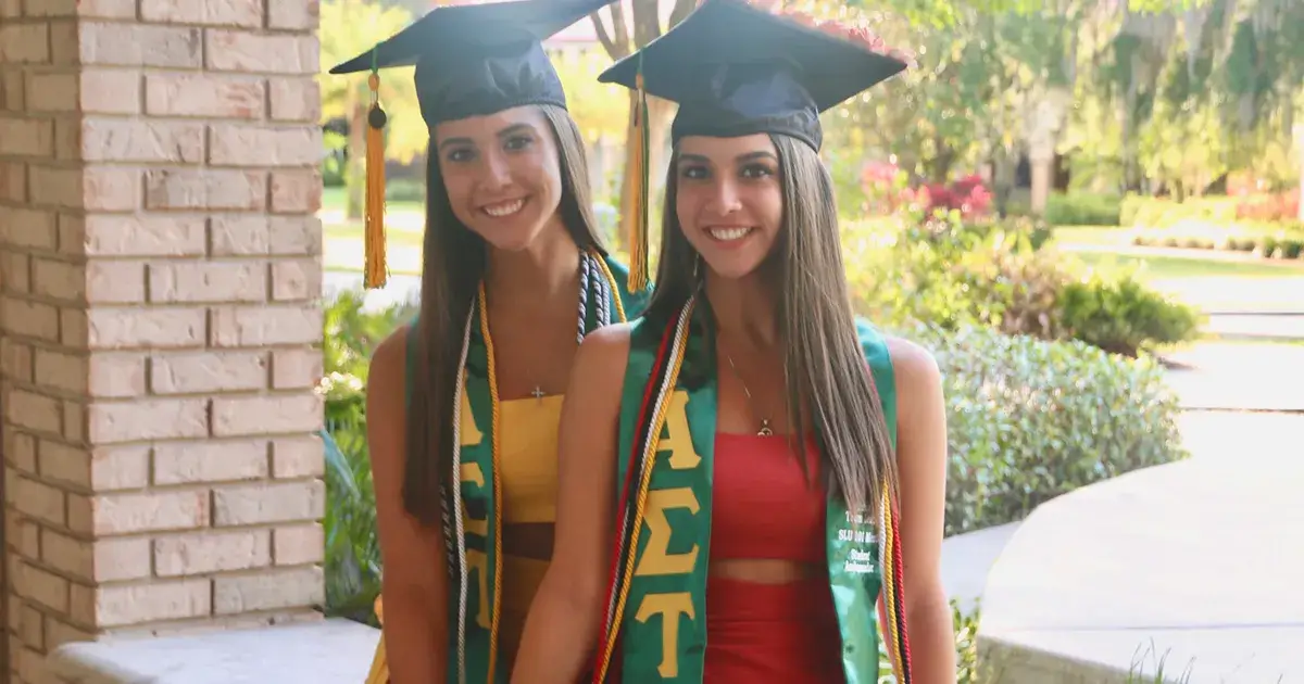 A photo of Jenna and Jessica Skrelunas, identical twin sisters, at the 2021 Saint Leo University commencement ceremony at which they earned their bachelor's degrees from University Campus; they are wearing their cap and gown