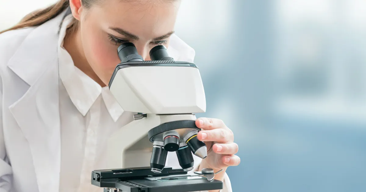 A photo of a woman using a microscope to demonstrate someone looking closely at something for the blog article on how to research a company for a job interview