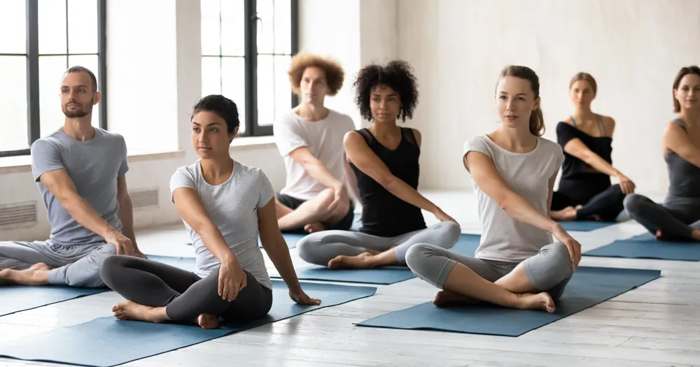 A photo of a group yoga class with several people doing various yoga poses for the blog article on the best yoga poses for stress management when pursuing a college degree