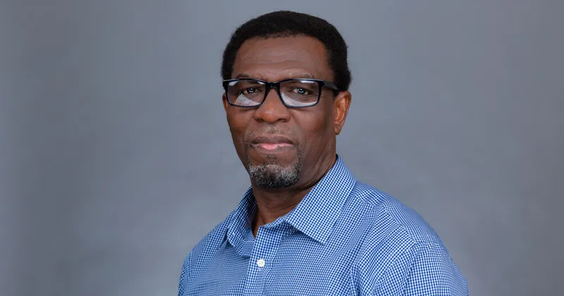 A head shot of Okey Igbonagwam, a Saint Leo University computer science professor, wearing glasses and a blue dress shirt; Igbonagwam is an African-American man with a beard