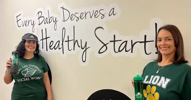 A photo of Mary Martinez-Drovie and Maria Dacosta, two Saint Leo University alumni, dressed in Saint Leo gear standing next to a Healthy Start Coalition sign where they both work; both are holding Saint Leo tumblers as well, and both have gone on to rewarding careers in helping professions