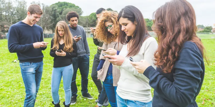 A photo of a group of several college students standing in a grassy field looking at their phones; this is for the blog article on the best apps for college students with ADHD