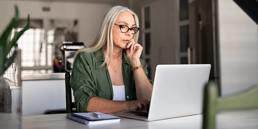 A photo of a Caucasian woman with blond hair sitting at a desk and working on a laptop in her home office for the blog article on handy hints at succeeding at a doctorate dissertation