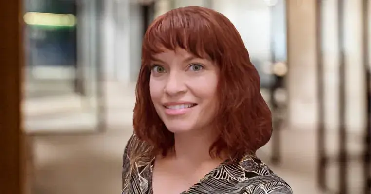 A photo of Amy Harris, an instruction and assessment librarian, in the Daniel A. Cannon Memorial Library at Saint Leo University; she has shoulder-length, brunette-colored hair and is wearing a floral dress and smiling; Harris serves as an embedded librarian for various Saint Leo courses