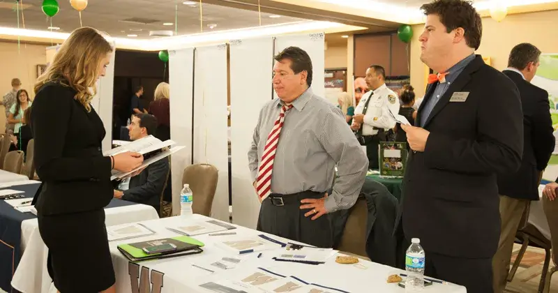 A photo of several Saint Leo University students dressed in business casual attire networking with employers at tables at a career fair held at University Campus for the blog article on tips for networking in college