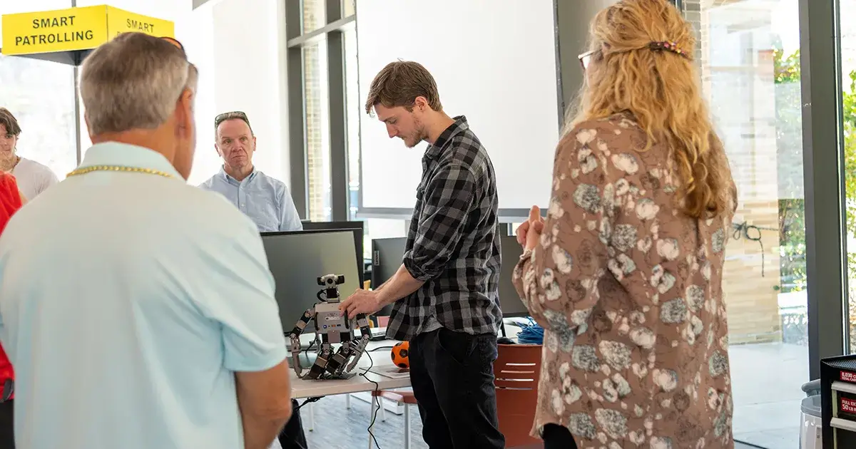 A photo of a Saint Leo University student working with a robot in the robotics lab at University Campus with a group of people watching; this is for the blog article on the top careers in robotics