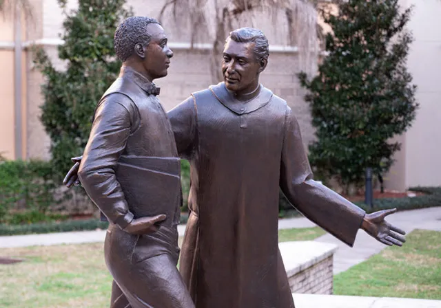 image of statue depicting a priest talking with a student