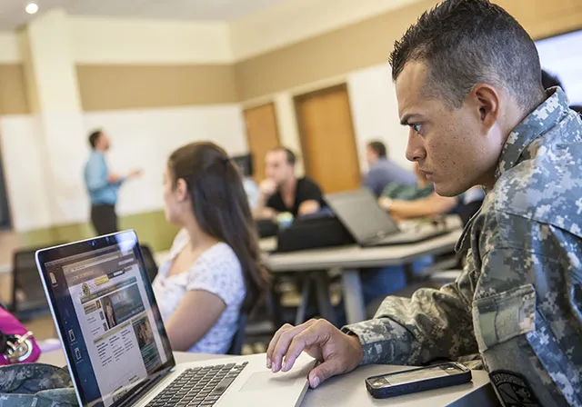 Military student in works on laptop in classroom.