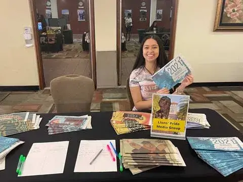 A photo of Isa Riano, a rising Saint Leo University junior, sitting at a table on University Campus during the 2022 MANE Event in which new and prospective students attended to learn more about the university and its programs; she was representing the Lions’ Pride Media Group where she works as the advertisement manager for the student newspaper.