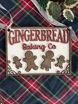 A photo of a square wooden ornament that says ‘Gingerbread Baking Co.’ with several little Gingerbread people under the text; this was designed by Saint Leo University business administration degree student Brianna Adeeb for her Etsy store