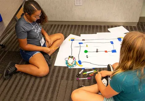 Desirae Gardner and Rosalyn Fletcher work with robot on board game-like surface