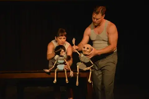 A photo of Erin Austin, an adjunct theatre degree professor at Saint Leo University, on stage with two actors with puppets performing in “Table for Two” written by Austin and commissioned by Bare Theatre Company; it was first performed at the Borderlight Theatre Festival in Cleveland, OH in 2019
