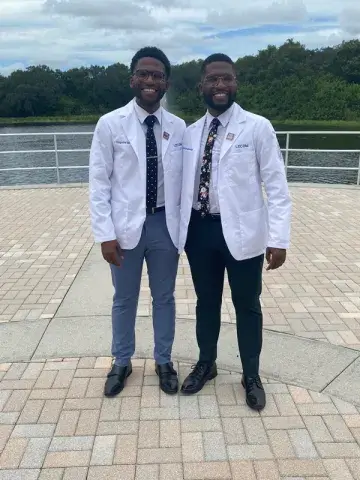 A photo of Chidozie and Chigozie Igbonagwam, identical twins who are both alumni of the Saint Leo biology degree program, dressed up in suits and standing outside on a patio