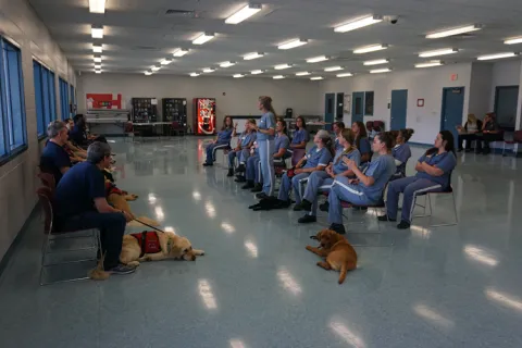 A photo of military veterans training with inmate-trainers in the WOOF Prison Program through Patriot Service Dogs at the Lowell Correctional Institution in the Ocala area of Marion County, FL; Julie Sanderson, a Saint Leo MSW alumna, operates Patriot Service Dogs