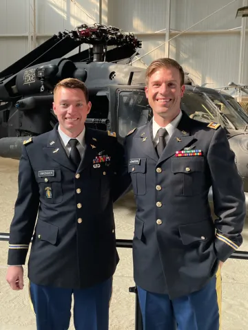 A photo of James “Dakota” Swonger, an alumnus of Saint Leo University and the Saint Leo ROTC program, posing with an Army officer and a helicopter in the background; this photo was taken at Dakota’s aviation captain’s career course graduation